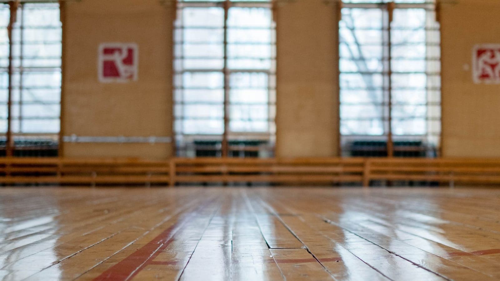 Eine leere Turnhalle mit Parkettboden, im Hintergrund hohe Fenster im Gegenlicht.